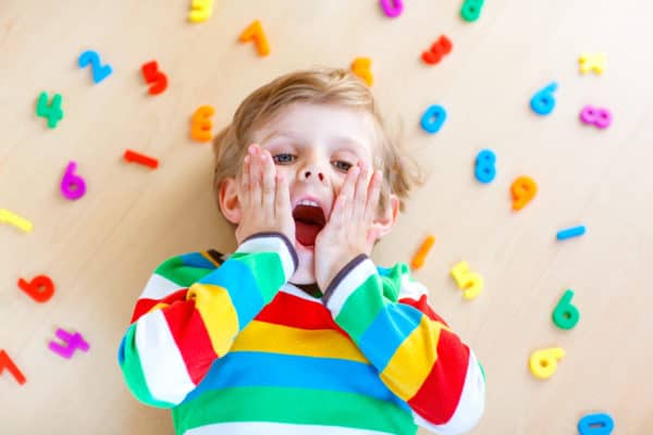 Child playing with colourful numbers and letters on the floor.