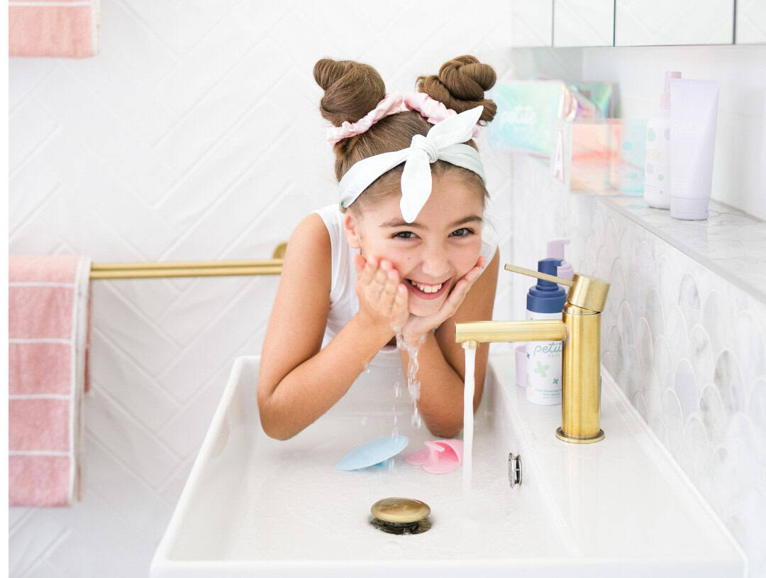Happy pre-teen girl washing her face with skincare products in the bathroom.