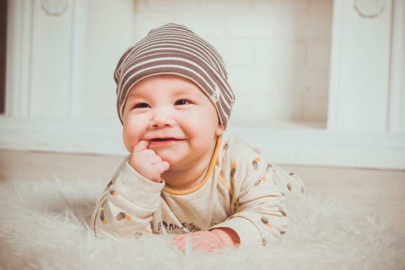 Baby lying on the floor with a striped hat, smiling and looking curious. Perfect for family, parenti.