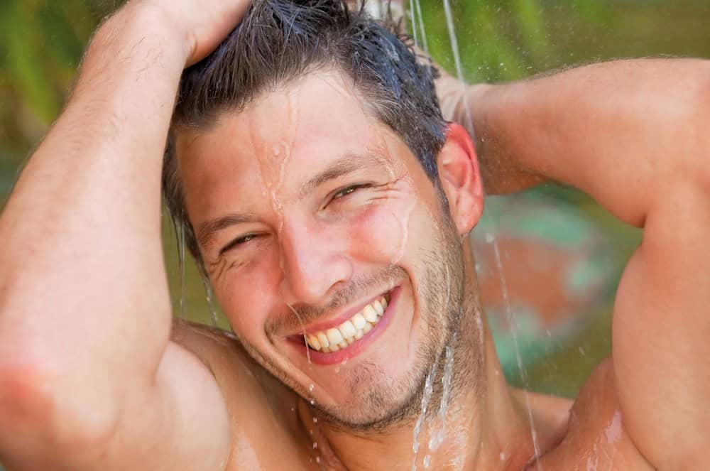 Happy man rinsing hair with homemade shampoo outdoors, smiling and enjoying clean hair.