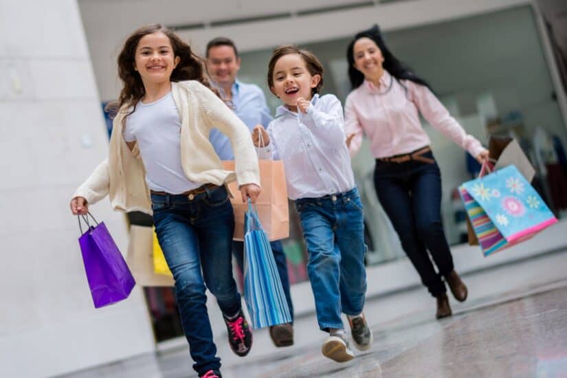 Family shopping at the mall with kids carrying shopping bags.