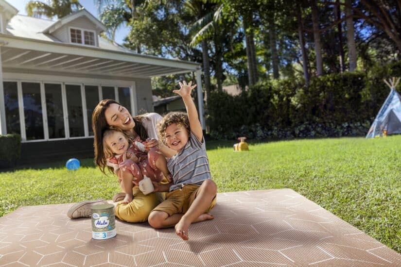 Family playing on a picnic blanket in the garden with children smiling and having fun.