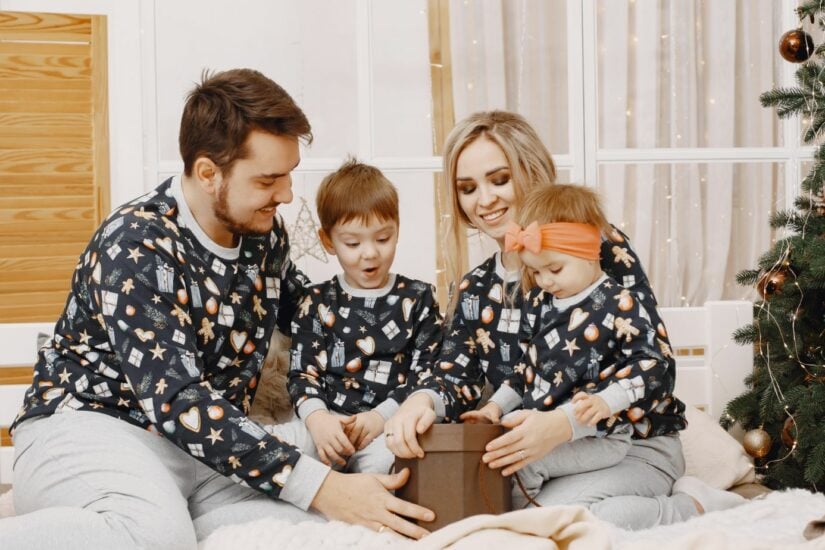 Family opening Christmas gift with children and parents in cozy holiday pajamas.