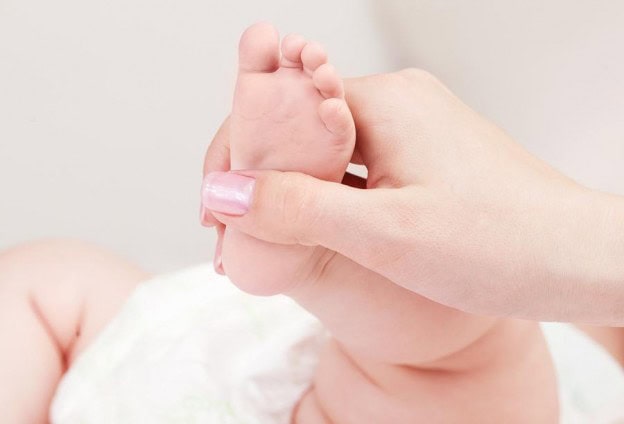 Close-up of a baby's foot being gently held by an adult hand for soothing sleep.