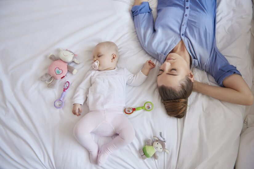 Mother and baby sleeping peacefully on bed with toys nearby.