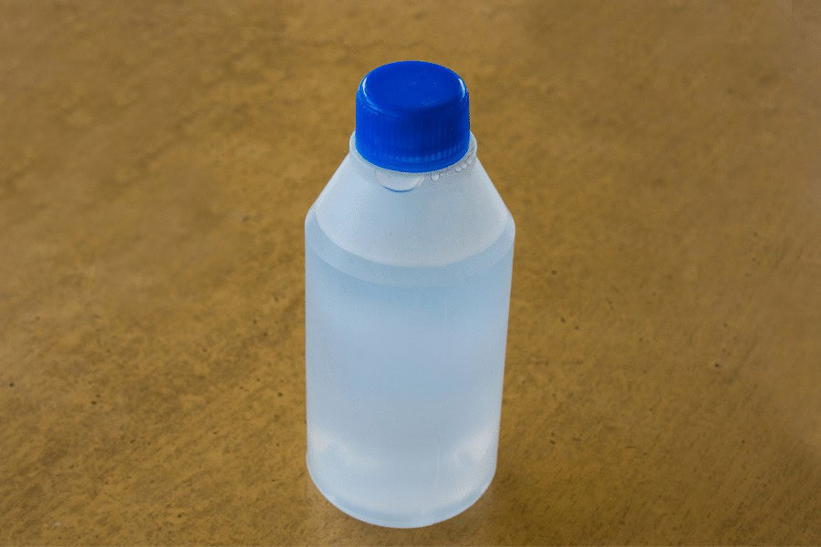 Clear plastic bottle of hydrogen peroxide with blue cap on a brown surface.