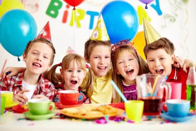 Kids celebrating birthday with balloons, cake, and party hats.