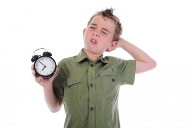 Child looking confused holding an alarm clock, illustrating time zone adjustment issues with childre.