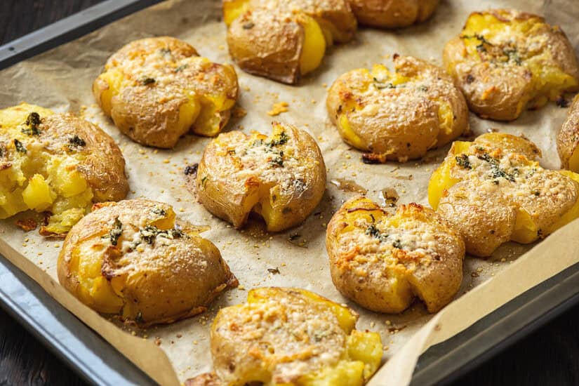 Delicious crispy smashed potatoes with herbs and seasoning on a baking tray.