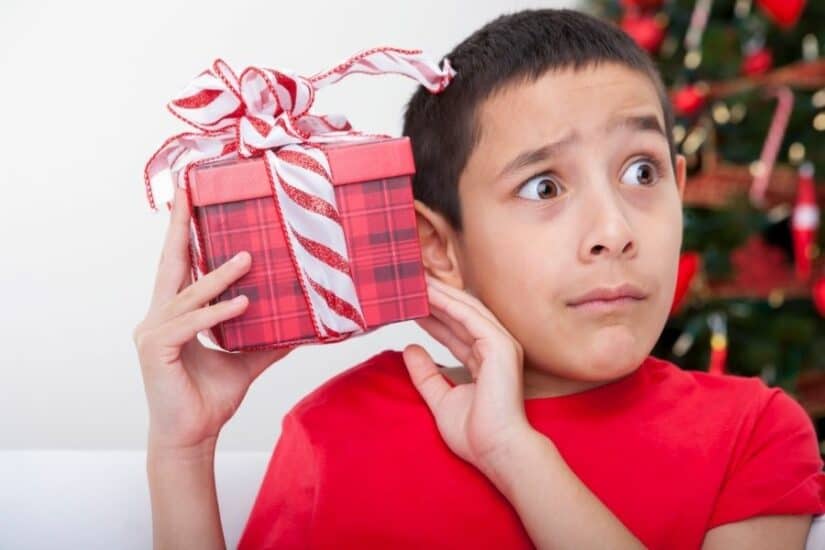 Child holding a wrapped Christmas gift with a surprised expression.