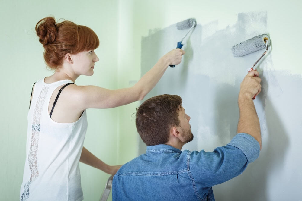 Woman and man painting wall with rollers, home interior renovation on a budget.