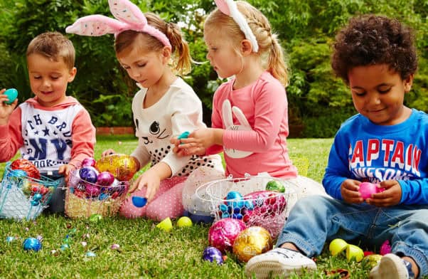 Easter egg hunt with children wearing bunny ears, collecting colourful eggs outdoors.