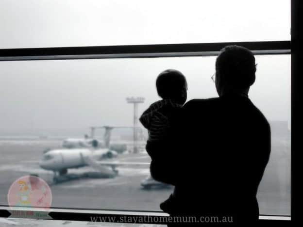 Parent waiting at airport window with child, facing airplane, symbolising FIFO worker concerns.