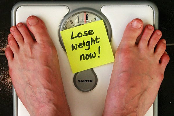 Bathroom scale with a "Lose weight now!" sticky note for weight loss motivation.