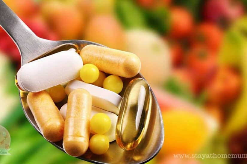 Assorted vitamins and supplements in a spoon with fresh produce background.