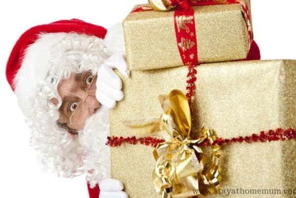 Santa peeking from behind Christmas presents, hiding gifts for kids.