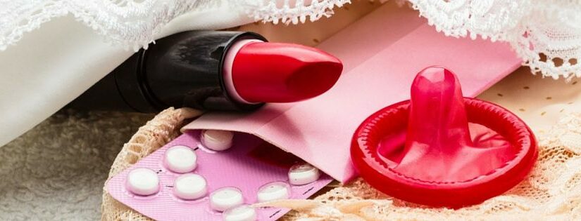 Close-up of a red condom and birth control pills on a lace cloth.