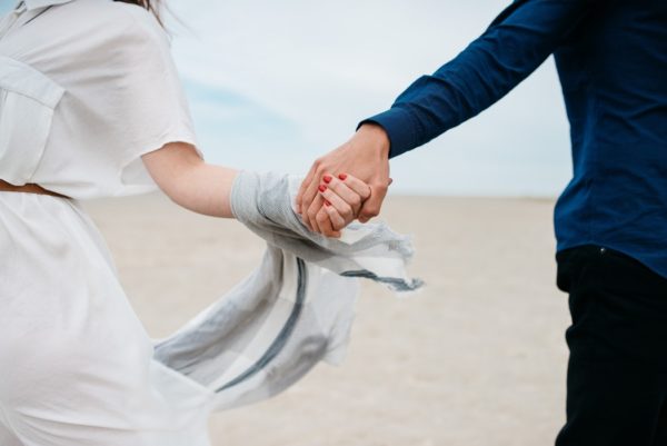 Close-up of a couple holding hands on the beach, symbolising love and connection.