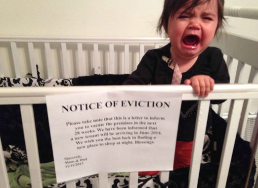 Baby crying in crib with eviction notice sign attached.