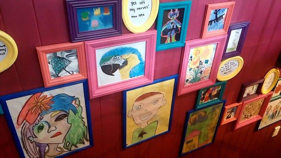 Colorful kids' artwork framed and arranged on a vibrant pink wall.
