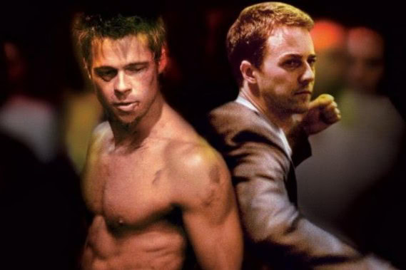 Two men, one shirtless and one in a suit, mimicking a fight scene in a playful setting.