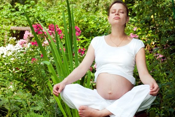 Pregnant woman meditating outdoors surrounded by lush greenery and vibrant flowers.