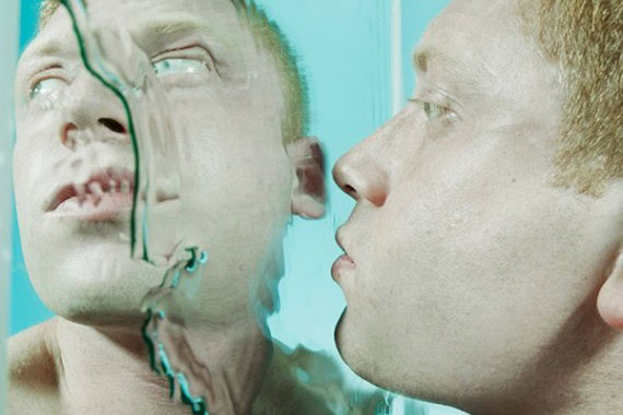 Man looking at his reflection in a mirror, exploring the idea of doppelgangers.