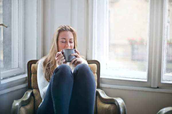 Relaxed woman enjoying a hot beverage in a cozy setting by the window.