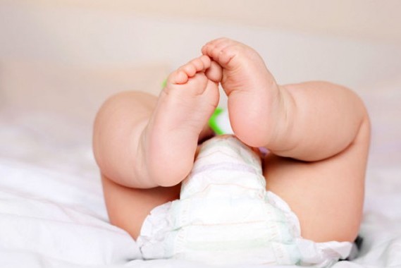Baby lying on back with legs up, wearing diaper, close-up of diaper area.