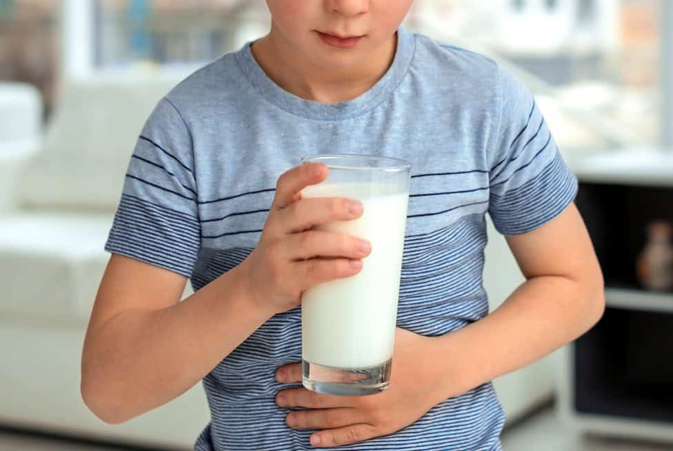 Child holding a glass of milk, possibly experiencing food sensitivities.
