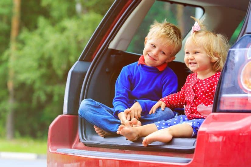 Happy kids sitting in the open trunk of a car during a fun road trip.