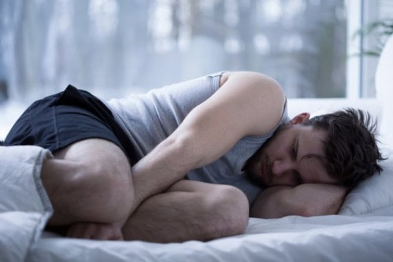 Man lying alone on bed, looking distressed, in a quiet bedroom setting.