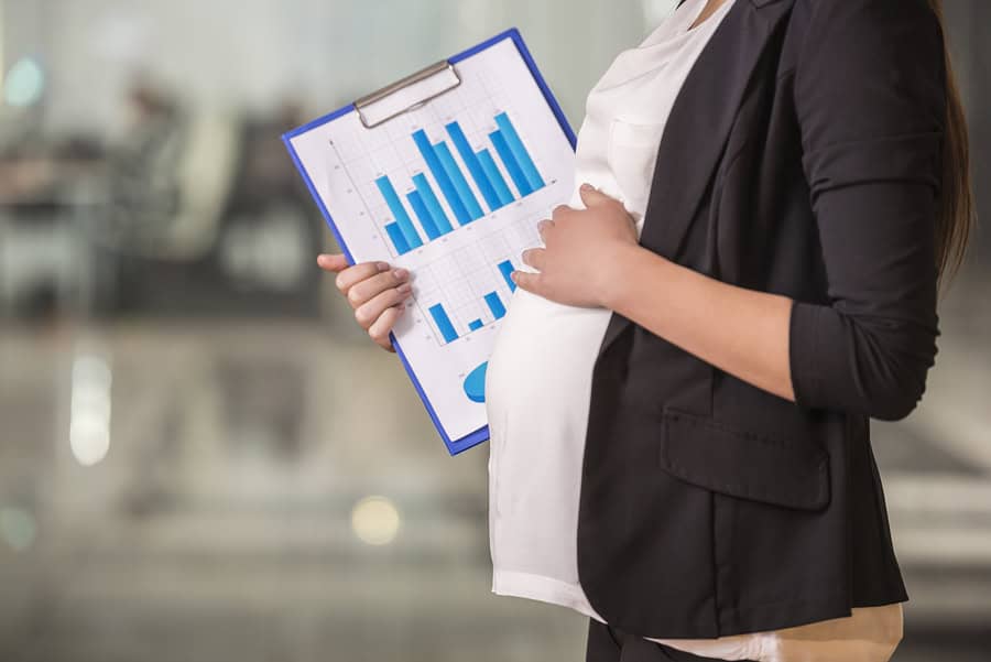 Pregnant woman holding financial charts in an office setting.