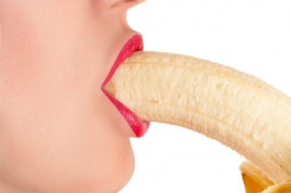 Woman with red lipstick holding a banana in her mouth for health benefits.