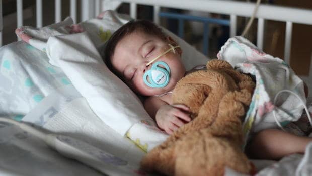 Young child in hospital with oxygen mask and teddy bear after heart transplant.