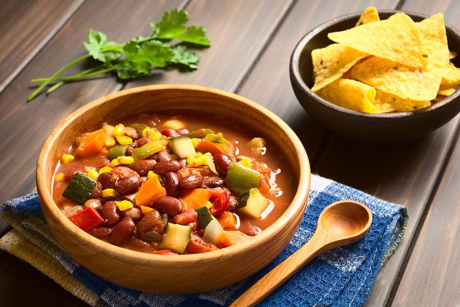 Vegetarian chili with beans, corn, and vegetables in a wooden bowl.