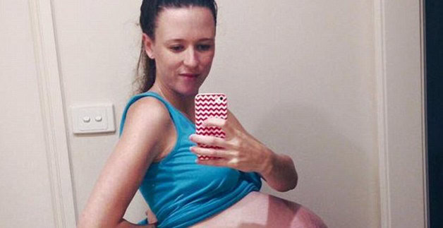 Pregnant woman taking mirror selfie to showcase her baby bump.