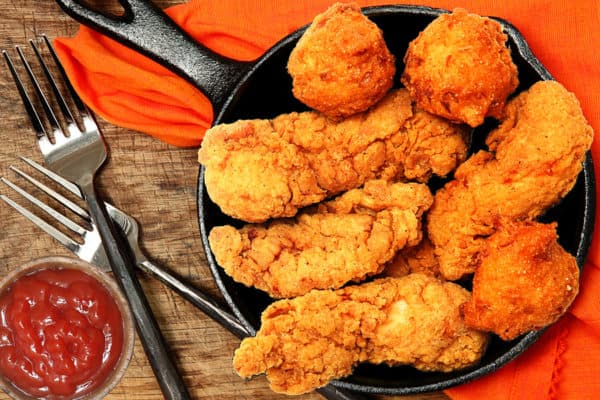 Hot and spicy chicken tenders in a skillet with dipping sauce.