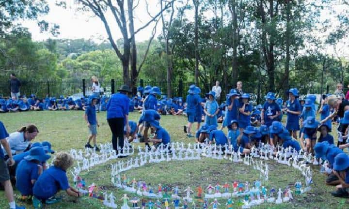 Children planting paper flowers at outdoor school event in blue uniforms.