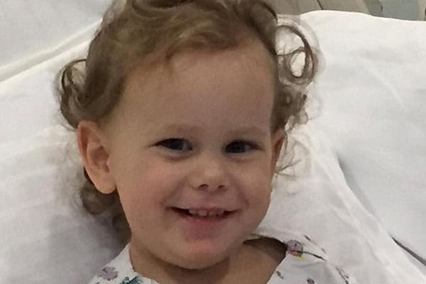 Girl smiling in hospital bed following a rare flesh-eating bacteria illness.