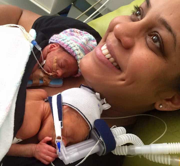 Adorable premature twins holding hands in hospital, showcasing their strong bond and resilience.