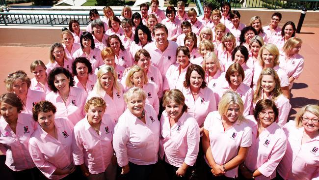 Group of women in pink shirts smiling outdoors on tennis court.