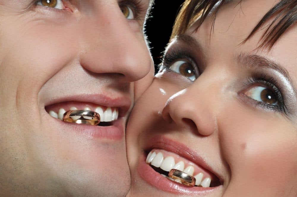 Quirky wedding photo featuring couple with gold teeth and playful expressions.