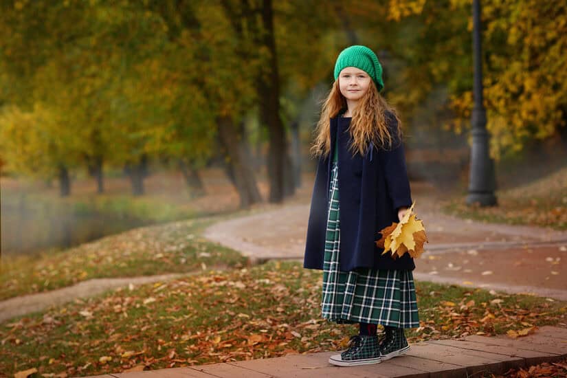 Girl holding autumn leaves in a park during fall.