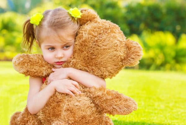 Young girl hugging a teddy bear outdoors, symbolising comfort after pet loss.