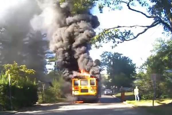 Bus on fire with thick black smoke billowing out, driver risking lives to rescue children.