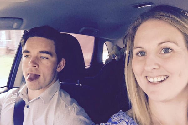 Happy couple in car, with dad driving and mum smiling, celebrating stay-at-home parenting.