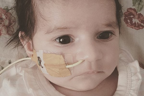 Baby with nasal oxygen tube and medical tape on face in hospital.