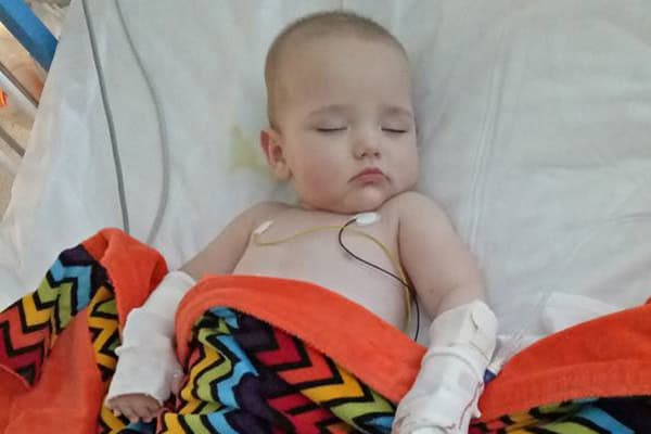 Child resting in hospital bed with medical tubes after illness from contaminated trolley.