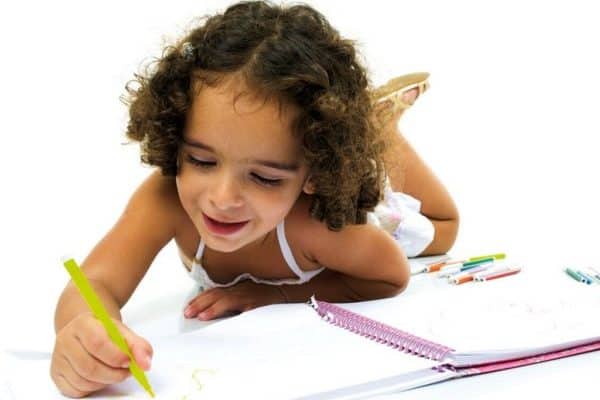 Child drawing with markers on paper for preschool readiness.